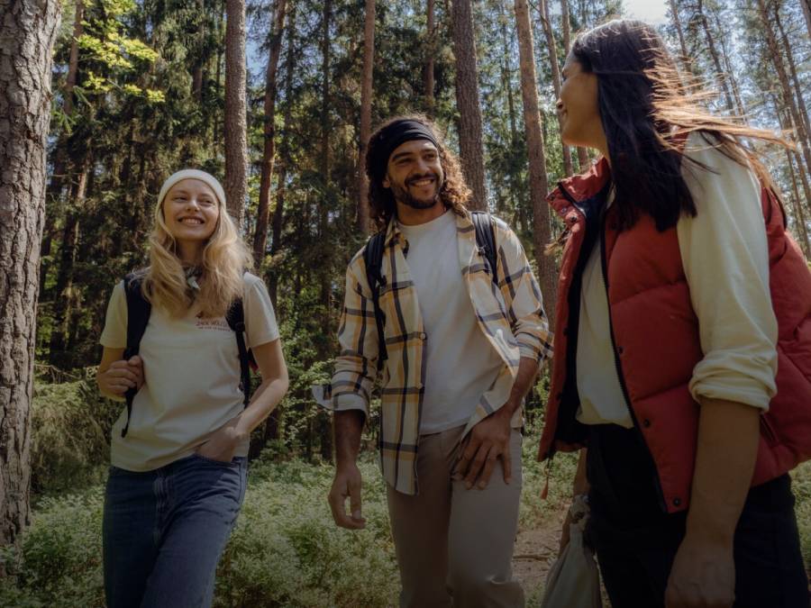 Trois randonneurs souriants en tenue de randonnée automnale décontractée dans une forêt ensoleillée